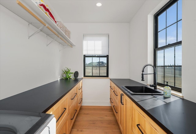 kitchen with dark countertops, light brown cabinetry, recessed lighting, light wood-style floors, and a sink