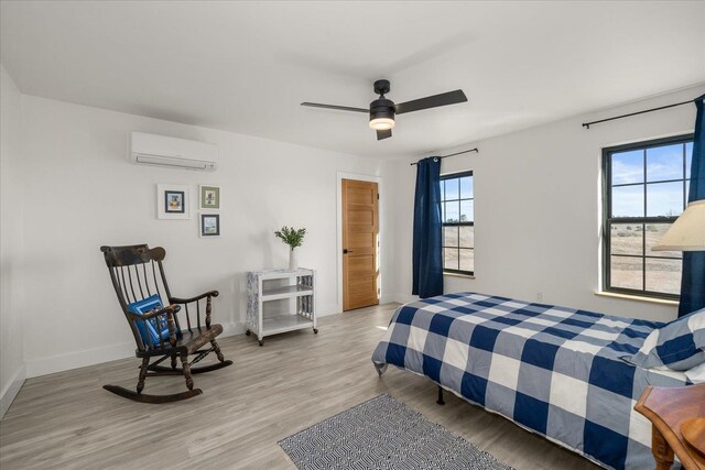 bedroom with baseboards, light wood-type flooring, a wall unit AC, and a ceiling fan