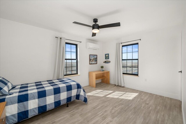 bedroom with ceiling fan, baseboards, an AC wall unit, and wood finished floors