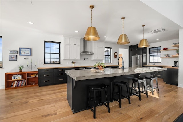 kitchen with visible vents, a sink, white cabinetry, high quality fridge, and wall chimney range hood