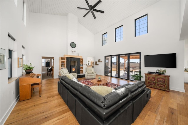 living area with baseboards, a warm lit fireplace, wooden ceiling, light wood-style floors, and a ceiling fan