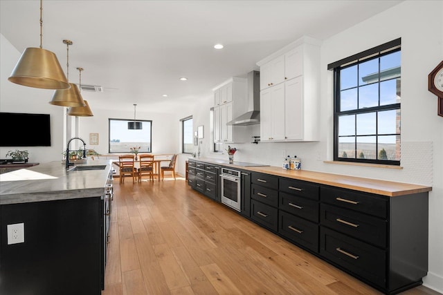 kitchen featuring oven, dark cabinetry, wall chimney exhaust hood, and a sink