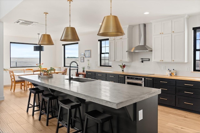 kitchen featuring dark cabinetry, oven, a sink, white cabinets, and wall chimney exhaust hood