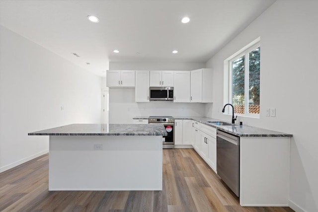 kitchen with light wood-type flooring, a sink, dark stone countertops, a kitchen island, and stainless steel appliances