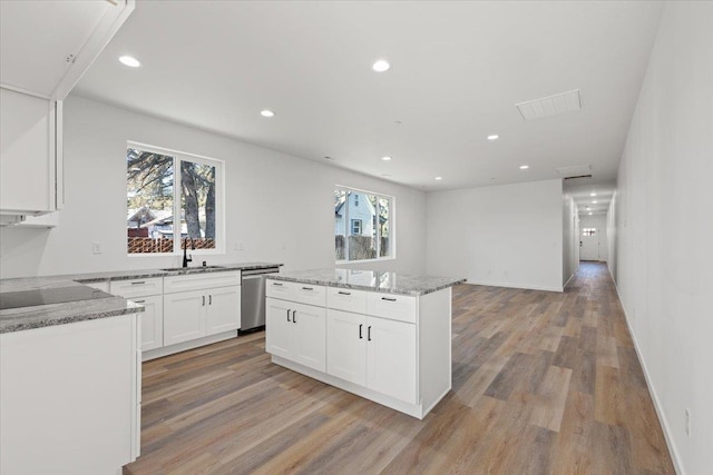 kitchen featuring light stone counters, dishwasher, a center island, and a sink