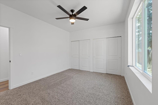 unfurnished bedroom with two closets, baseboards, multiple windows, and carpet