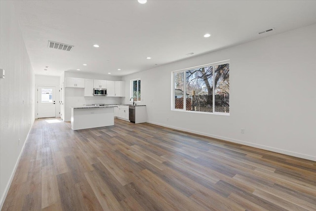 kitchen featuring visible vents, open floor plan, wood finished floors, white cabinetry, and stainless steel appliances