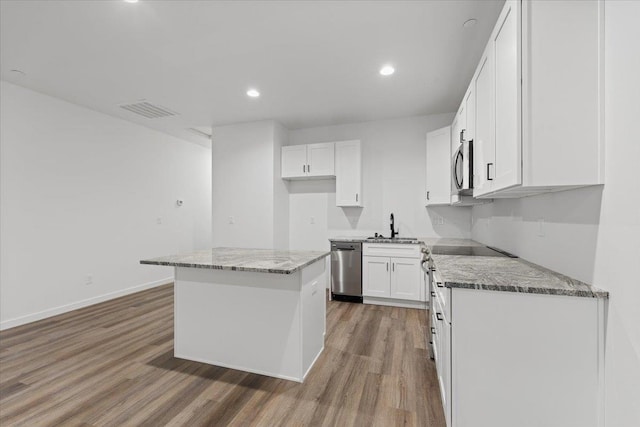 kitchen with visible vents, a sink, appliances with stainless steel finishes, light wood finished floors, and light stone countertops