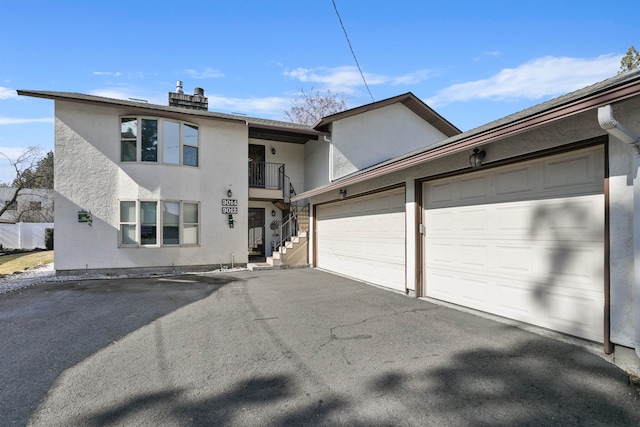 view of front facade with stucco siding, a balcony, a garage, and driveway