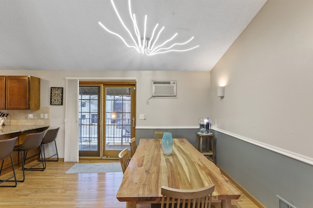 dining room with light wood finished floors, visible vents, an inviting chandelier, a textured ceiling, and a wall mounted AC