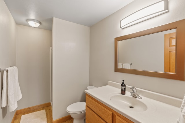 bathroom with vanity, toilet, wood finished floors, and baseboards