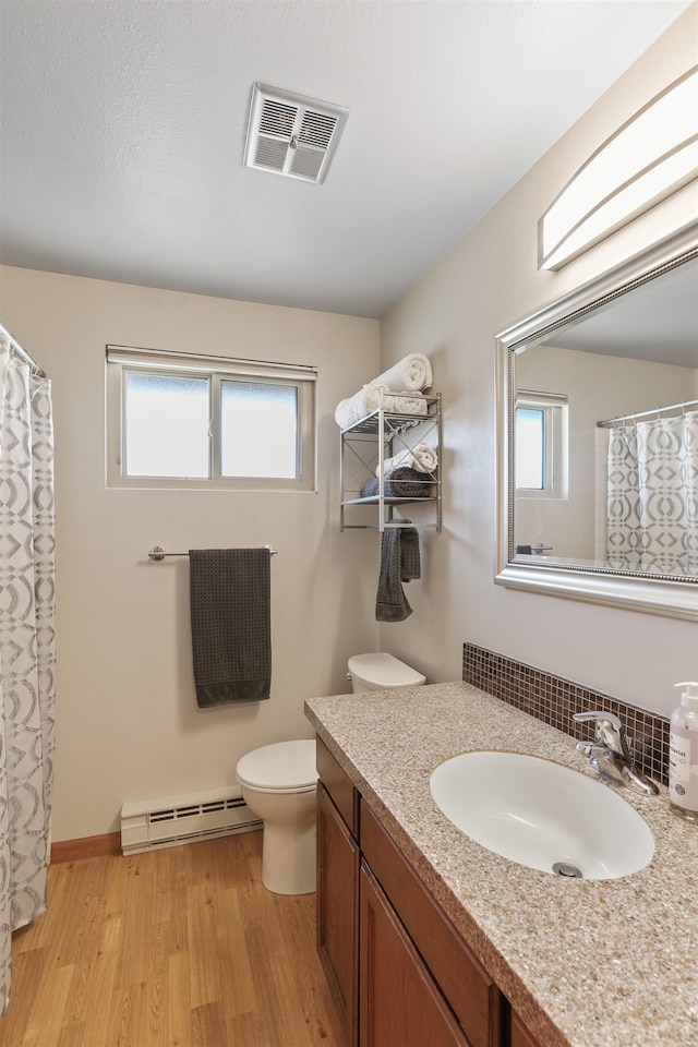 full bath with visible vents, a baseboard heating unit, toilet, wood finished floors, and vanity