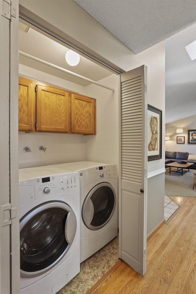 laundry area with cabinet space, washer and dryer, a textured ceiling, and light wood-style floors