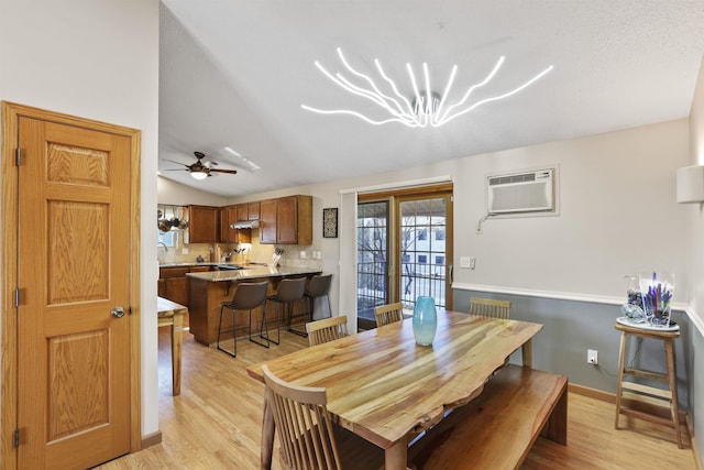 dining space with baseboards, a wall unit AC, light wood-style flooring, and vaulted ceiling