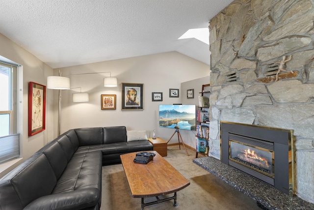 living room with a stone fireplace, vaulted ceiling with skylight, carpet, and a textured ceiling