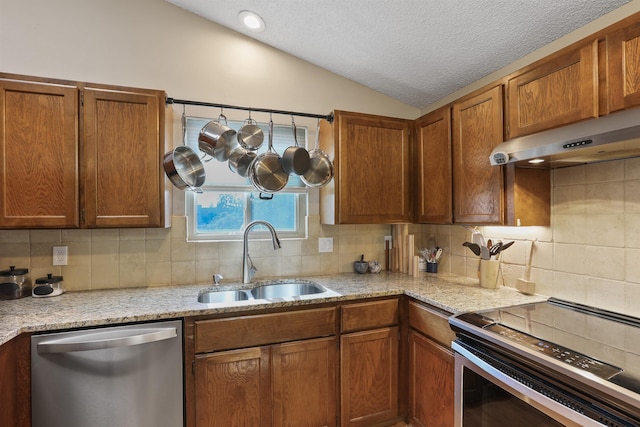 kitchen with lofted ceiling, a sink, decorative backsplash, under cabinet range hood, and appliances with stainless steel finishes