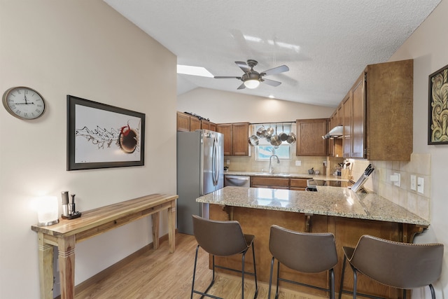 kitchen with tasteful backsplash, under cabinet range hood, light stone counters, appliances with stainless steel finishes, and a peninsula