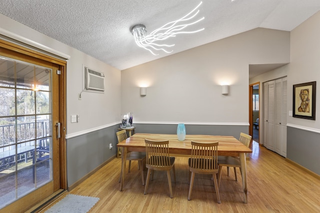 dining room with a textured ceiling, a wall mounted air conditioner, light wood-style floors, and lofted ceiling