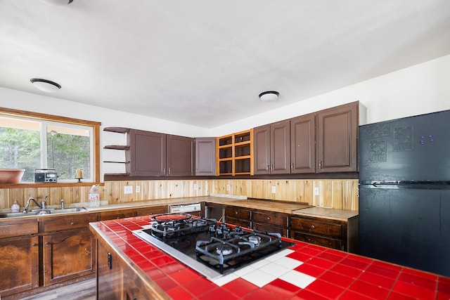 kitchen featuring black appliances, a sink, open shelves, glass insert cabinets, and tile counters