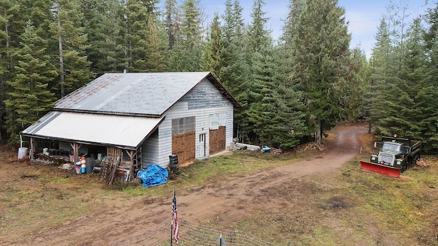 exterior space featuring metal roof, an outbuilding, a wooded view, and dirt driveway