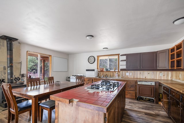 kitchen with tile countertops, stainless steel gas cooktop, dark wood finished floors, a sink, and glass insert cabinets