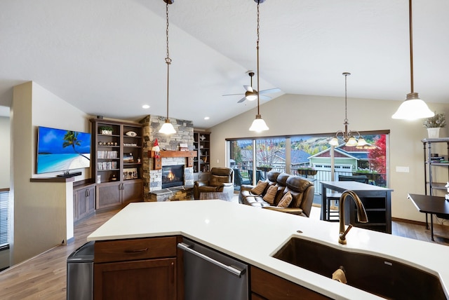 kitchen featuring light wood finished floors, dishwasher, light countertops, a stone fireplace, and a sink