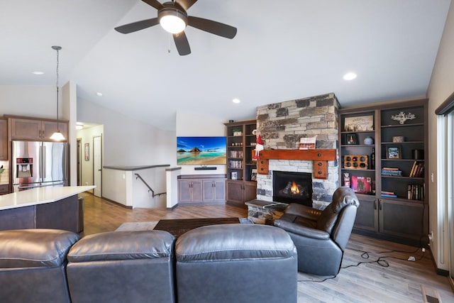 living room with a ceiling fan, visible vents, a stone fireplace, vaulted ceiling, and light wood-style floors