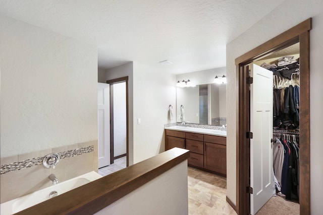 bathroom with a spacious closet, vanity, and a garden tub