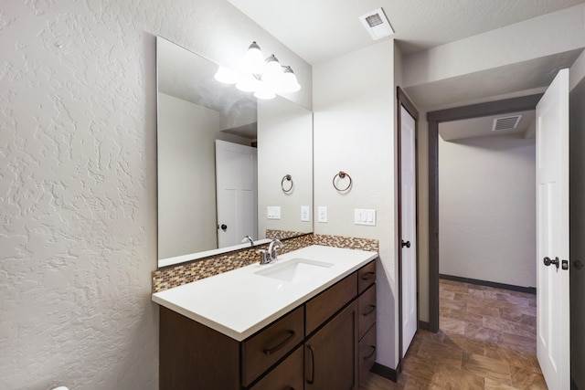 bathroom featuring visible vents, baseboards, vanity, and a textured wall