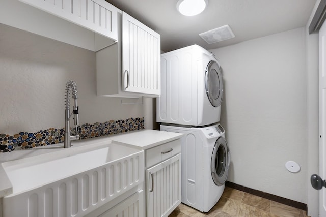 laundry room with baseboards, cabinet space, stacked washer / drying machine, and a sink