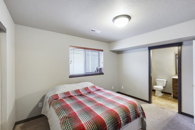 bedroom with baseboards, visible vents, ensuite bath, a textured ceiling, and light carpet