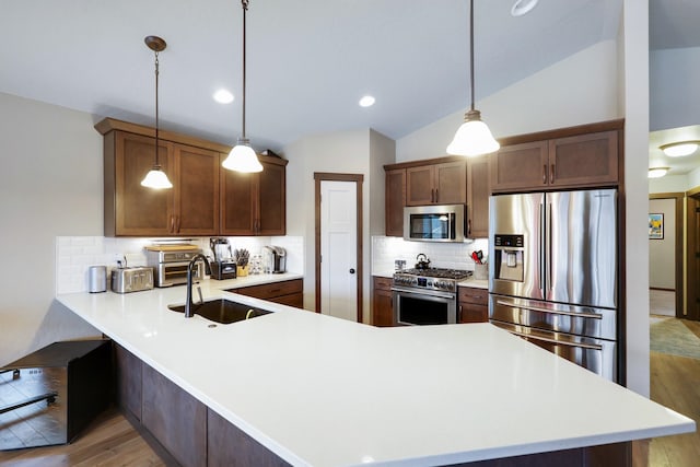 kitchen with a sink, stainless steel appliances, a peninsula, light countertops, and vaulted ceiling