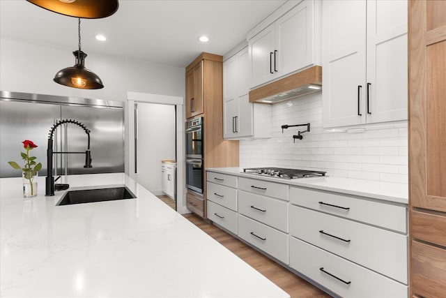 kitchen featuring a sink, hanging light fixtures, stainless steel appliances, light wood-style floors, and backsplash