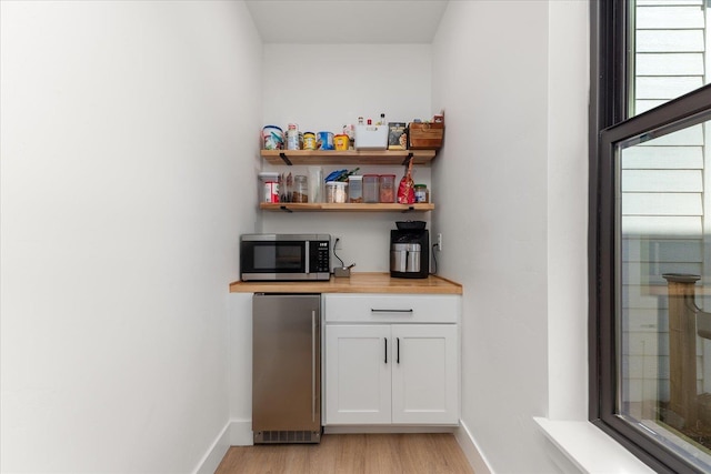 bar featuring light wood finished floors, stainless steel appliances, and baseboards