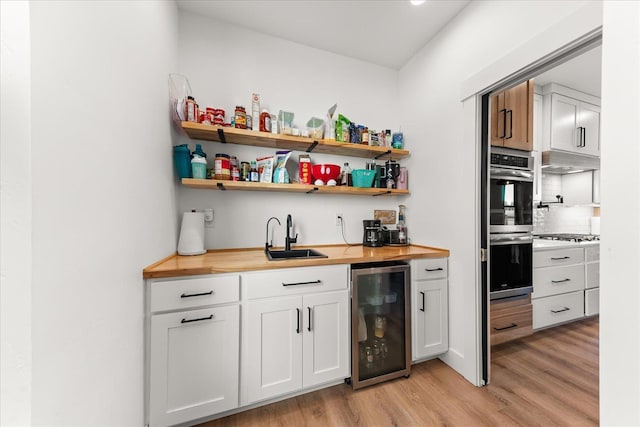 bar with light wood-style flooring, beverage cooler, appliances with stainless steel finishes, and a sink