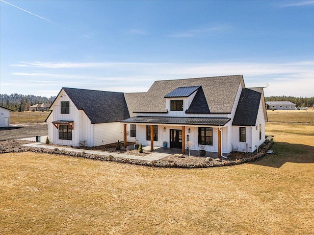 modern farmhouse with a standing seam roof, roof with shingles, board and batten siding, a front yard, and metal roof