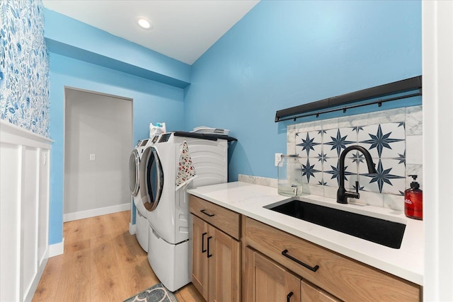 laundry area featuring baseboards, cabinet space, a sink, light wood-type flooring, and washer and clothes dryer