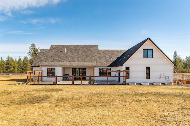 back of property with a wooden deck, a lawn, and a shingled roof