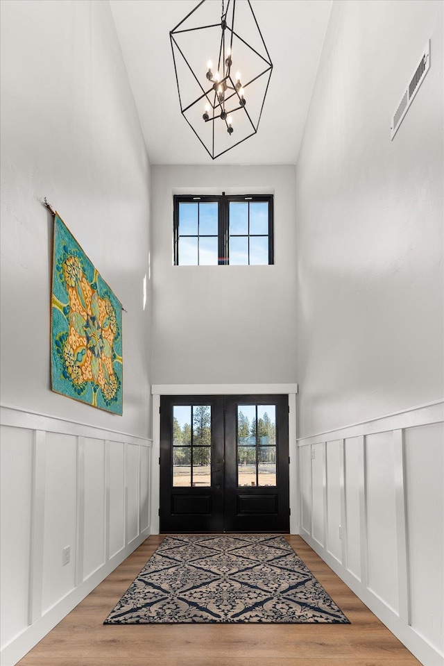 entrance foyer with visible vents, wood finished floors, french doors, wainscoting, and a chandelier