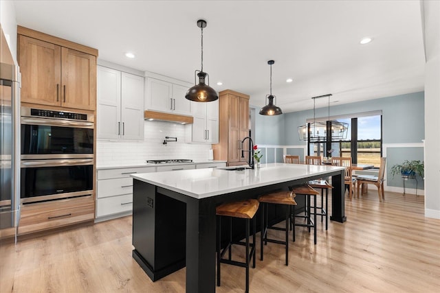 kitchen with light wood finished floors, backsplash, light countertops, appliances with stainless steel finishes, and a sink