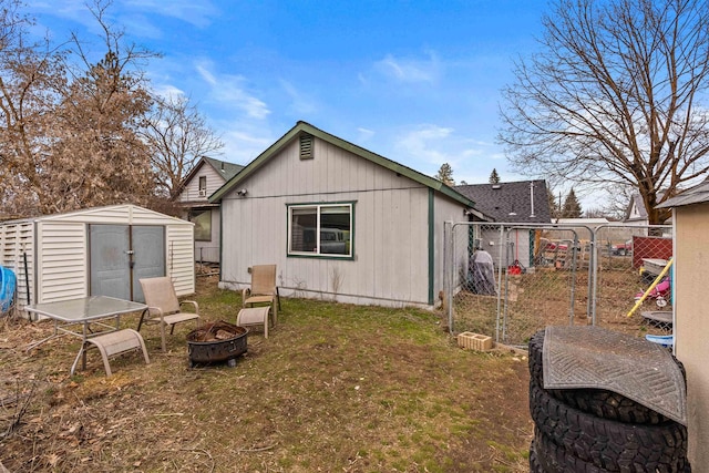 rear view of property featuring a storage unit, an outbuilding, a lawn, fence, and an outdoor fire pit