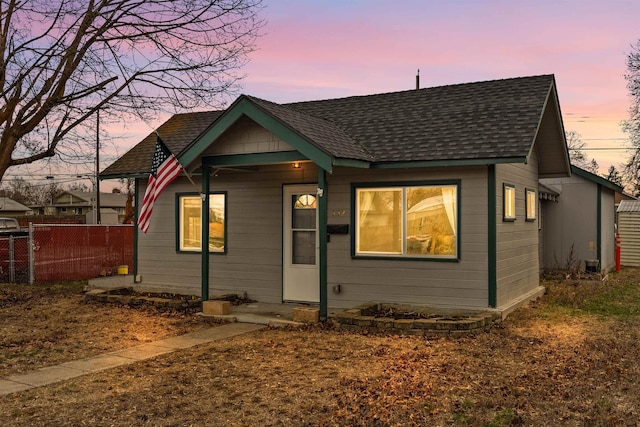 bungalow-style home featuring a shingled roof and fence