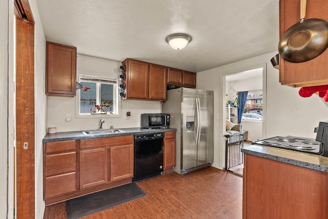 kitchen with dark countertops, dark wood finished floors, brown cabinets, black appliances, and a sink