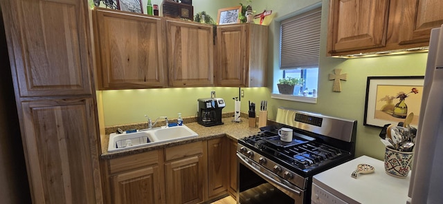 kitchen featuring gas range, brown cabinets, freestanding refrigerator, and a sink