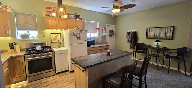 kitchen with a ceiling fan, freestanding refrigerator, a breakfast bar area, black microwave, and stainless steel range with gas stovetop