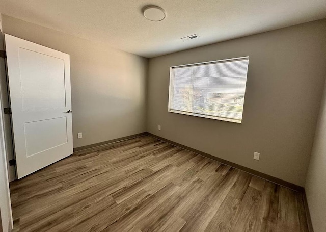 unfurnished room with visible vents, a textured ceiling, baseboards, and wood finished floors