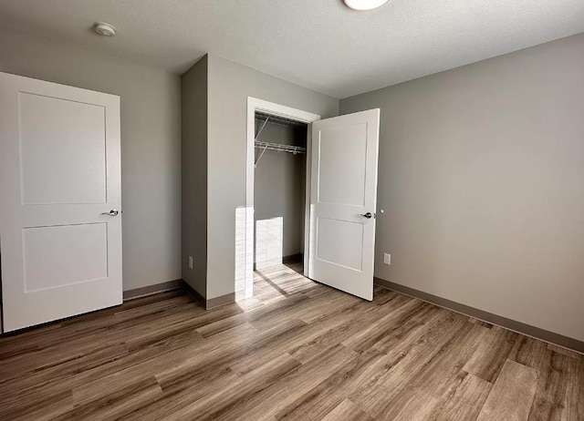 unfurnished bedroom featuring a closet, baseboards, a textured ceiling, and light wood finished floors