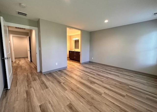 unfurnished bedroom with ensuite bath, visible vents, baseboards, and light wood-style floors