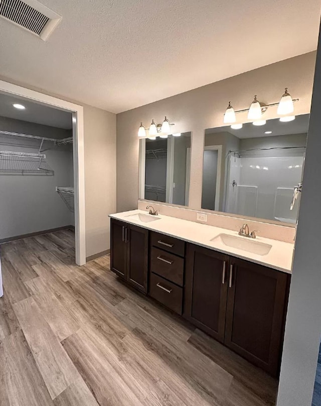 bathroom with wood finished floors, visible vents, double vanity, a sink, and a textured ceiling