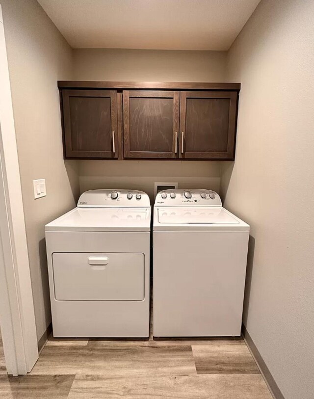 laundry area with washer and clothes dryer, cabinet space, light wood-type flooring, and baseboards